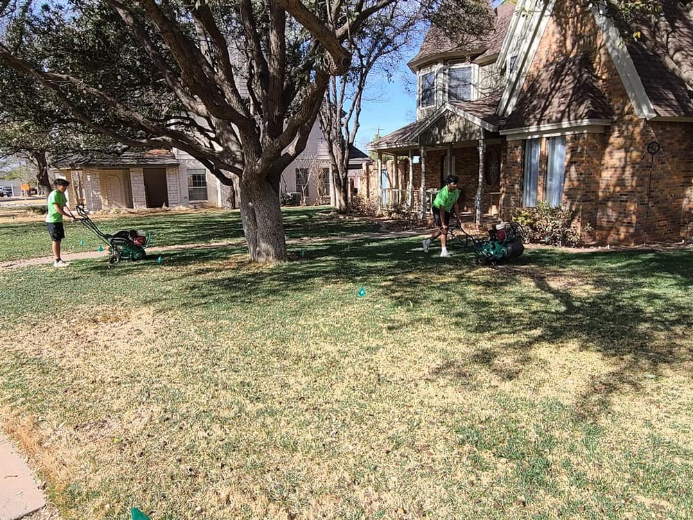 Two Bold Gold crew members running core aerators across a Midland front lawn